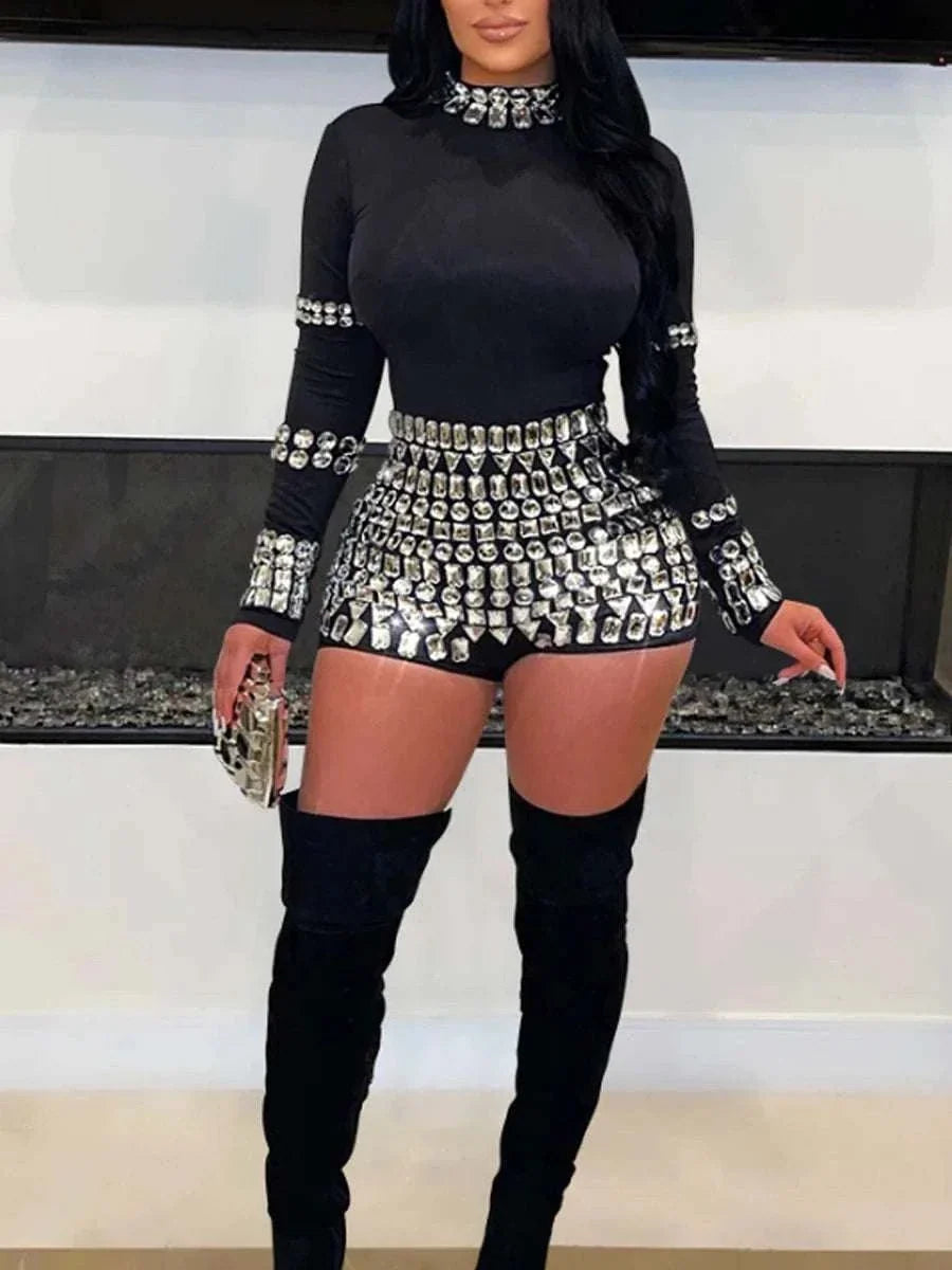 Black long-sleeve romper with a high neckline and silver rhinestone embellishments; Long Sleeve Rhinestone Decor accents trim the waist and shorts.