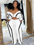 UnWritten Style two-piece tracksuit in white stretch fabric with bold black piping, an off-shoulder zip jacket and wide-leg pants.
