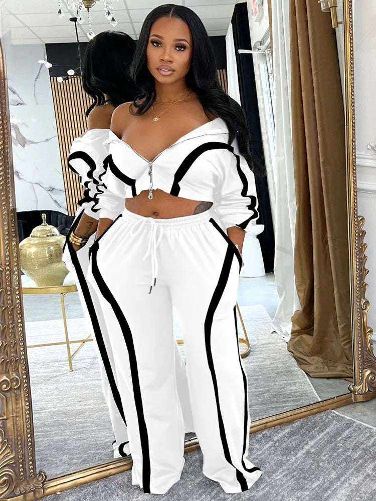 UnWritten Style two-piece tracksuit in white stretch fabric with bold black piping, an off-shoulder zip jacket and wide-leg pants.
