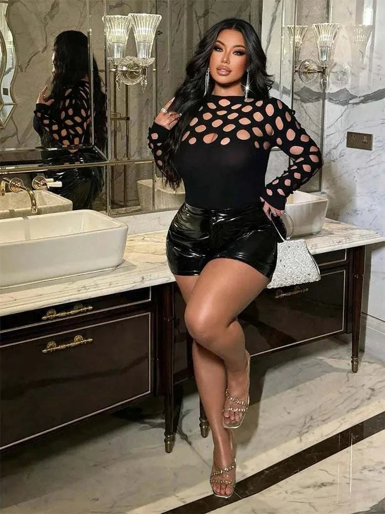 After Dark Allure Cutout Romper in black, with sheer-look long sleeves and oval cutouts, paired with glossy faux-leather shorts.